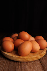 Brown eggs arranged in a rustic wooden plate over a dark wood table, highlighting the rising cost of eggs