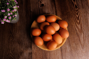 Wooden plate full of brown eggs on dark wooden table, concept of rising egg prices in the market