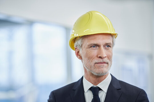 Thoughtful mature male manager wearing yellow hardhat in factory
