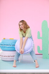 A young woman in a light casual outfit sits on a white step stool in a vibrant photo zone. She...