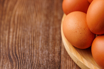 Wooden plate filled with brown eggs on dark wooden table, representing rising egg prices