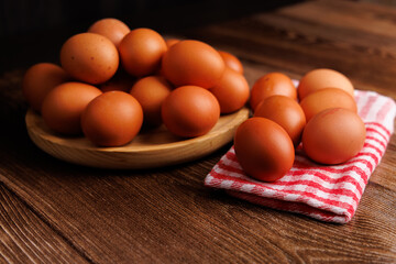 A wooden plate of brown eggs placed on a napkin-covered dark wooden table, highlighting the rising cost of food and groceries.