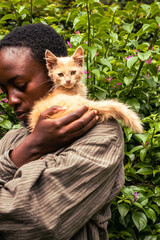 A young black woman standing outdoors with her kitten sitting on her shoulders