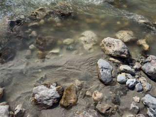 Obraz premium close-up view of rocks in crystal-clear river water. water ripples, water reflections. sunlight refraction. water pattern. abstract nature