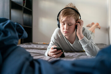 Portrait of boy with headphones lying on bed looking at cell phone