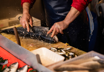 Fishmonger cleaning a large fish with water splashing around at a seafood market. Hands-on preparation of fresh fish in a traditional market environment.