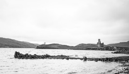 Black and white image of Loch Assynt with the ruins of Ardvreck castle in the background.