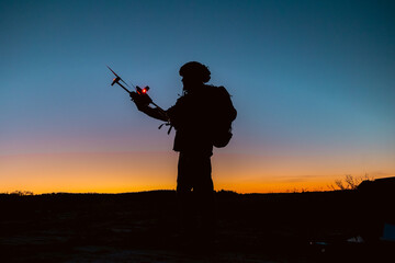 Silhouettes of soldiers are using drone for scouting during military operation against the backdrop...