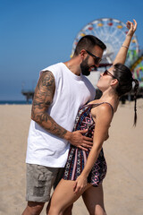 Close-up of young couple looking at each other closely and embracing while she lifts one arm, on the beach in Santa Monica, California.