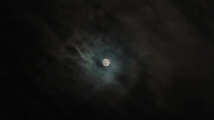 Full moon in a dark cloudy night sky. Clouds quickly fly past the Moon, giving an eerie feeling, like in thrillers and horror movies. Moonlight through black clouds. Real video footage