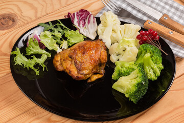 Serving of baked chicken thigh with vegetables on black dish