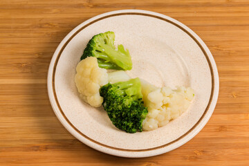 Boiled broccoli and cauliflower pieces on saucer on wooden surface