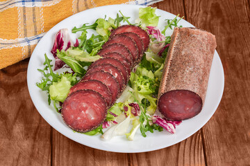 Partially sliced dry-cured sausage on leaf vegetables on dish