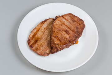Grilled pork steaks on white dish on a gray background