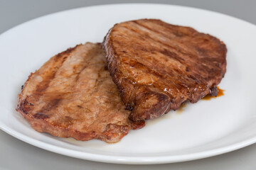 Grilled pork steaks on white plate, front view close-up