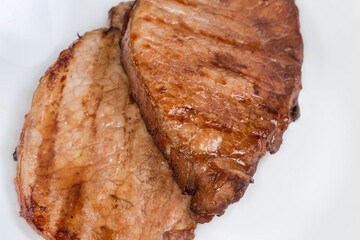 Grilled pork steaks on white plate, fragment close-up