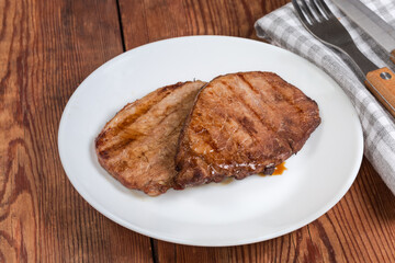 Serving of grilled pork steaks on rustic table close-up