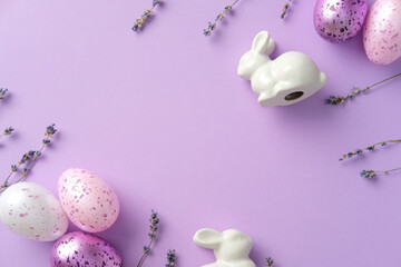 Easter flat lay composition with purple and white Easter eggs, ceramic bunnies, lavender flowers on pastel purple background.