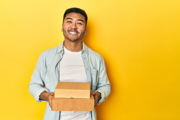 Asian man holding delivery food boxes, yellow studio backdrop happy, smiling and cheerful.