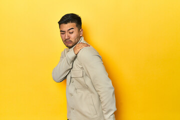 Fototapeta premium Asian man in stylish gray shirt on yellow studio having a shoulder pain.