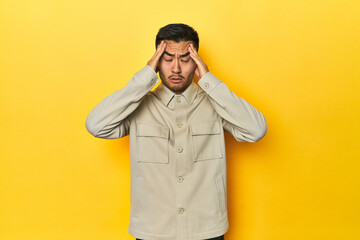 Fototapeta premium Asian man in stylish gray shirt on yellow studio touching temples and having headache.