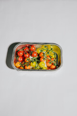 A tray of fruit with tomatoes, grapes, and oranges. The tray is in a white background