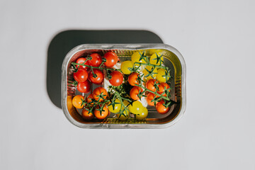 A tray of assorted colored tomatoes and grapes. The tray is silver and the tomatoes are red,...