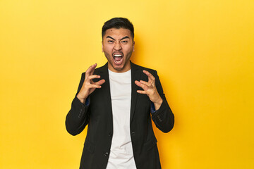 Asian man in black business jacket on yellow studio screaming with rage.