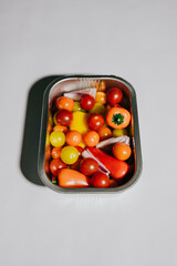 A metal tray full of assorted vegetables including tomatoes, peppers, and onions. The tray is on a white background