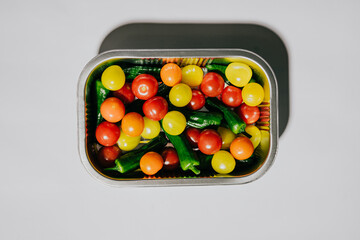 A tray of assorted fruits and vegetables, including tomatoes, peppers, and cucumbers. The tray is open and the fruits and vegetables are visible