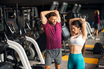 Fit Couple Stretching Together at a Modern Gym with Treadmills
