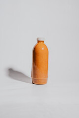 A bottle of orange juice is sitting on a white background. The bottle is tall and slender, with a white cap. Concept of freshness and health, as orange juice is often associated with vitamins