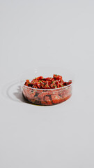 A bowl of red food is sitting on a white background. The bowl is made of plastic and is filled with red food
