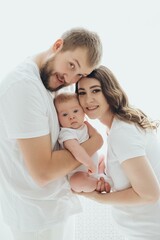 A happy young family mom dad and a small child smiling and kissing on a white isolated window background, a loving family threesome at home