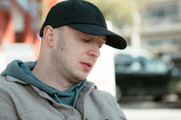 A young man in modern clothes with a cap on his head sitting and resting in cafeteria in a city...