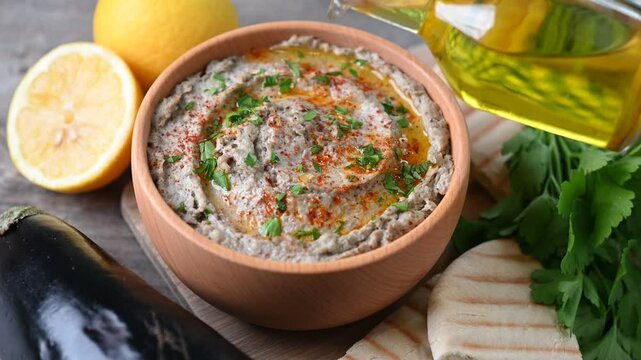 Pouring olive oil in traditional baba ganoush in bowl on wooden table