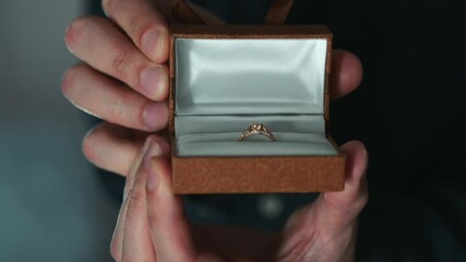 Wedding ring in a box.
A young guy opens a box with an expensive gold ring.
A gold ring with a shiny and expensive stone.
A diamond ring.
A diamond ring for a wedding