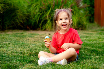 Little baby girl eating ice cream in summer on a green lawn grass, bright summer photo of a happy and laughing child with ice cream