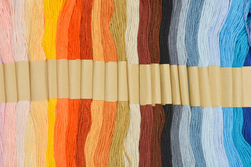 Rows of colorful embroidery floss are arranged in parallel and held together by cardboard holders