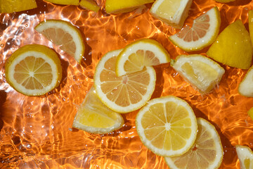 Slices of fresh lemons in water, splash of water, fresh orange background, top view