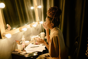 Woman preparing for performance in dressing room illuminated by stage lights, surrounded by makeup...