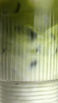 Matcha latte is stirred with ice. Close-up footage on the rotating table.