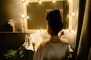 Individual with braided hair seen from behind holding documents and mobile device in dimly lit...