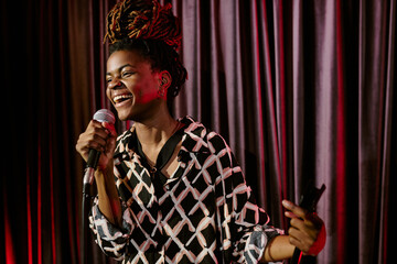 Smiling performer holding microphone while performing on stage. Vibrant energy and joy radiating...