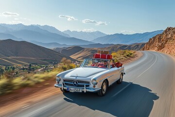 Fototapeta premium A vintage convertible car cruises down a winding road surrounded by majestic mountains and valleys. The clear sky and beautiful scenery enhance the classic driving experience.