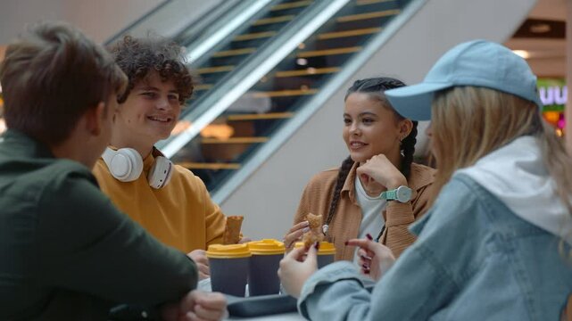 Happy relaxed teenage friends talking sitting in cafeteria of shopping mall