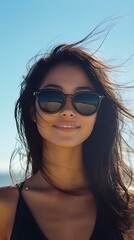 Fototapeta premium A beautiful woman with sunglasses smiling against a bright sunny beach backdrop, her hair flowing in the wind, capturing a carefree summer vibe.
