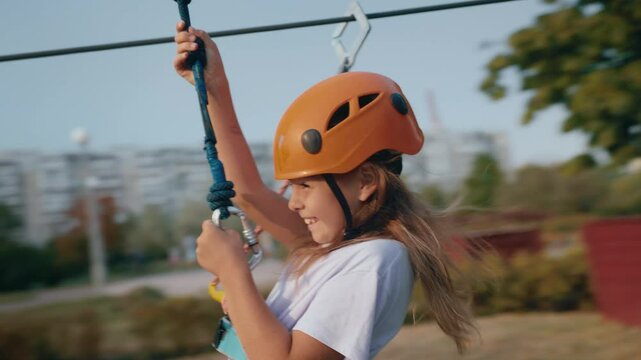 Joyful girl child going down zipline inclined rope with a suspended harness
