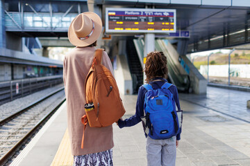 Mom and child with backpacks are waiting for the train on the platform. The family is ready to...