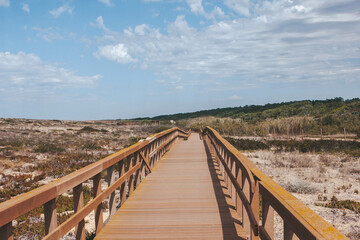 Obraz premium Wooden boardwalk over sandy dunes in Portugal, leading to the beach.